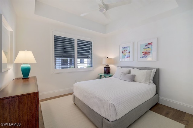 bedroom with light wood-type flooring, ceiling fan, and a tray ceiling