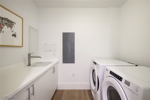 clothes washing area with sink, washing machine and clothes dryer, electric panel, cabinets, and light hardwood / wood-style flooring