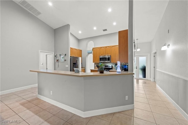 kitchen featuring a notable chandelier, appliances with stainless steel finishes, a high ceiling, kitchen peninsula, and light tile patterned flooring