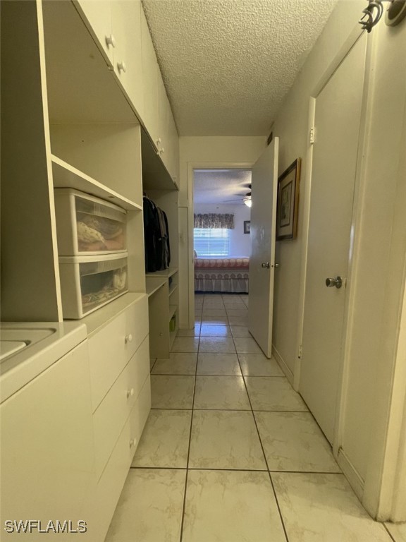 hall featuring a textured ceiling, washer / clothes dryer, and light tile patterned floors