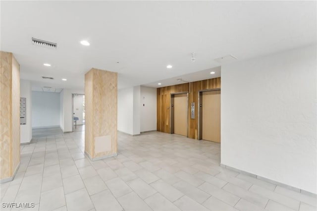 unfurnished room with elevator and wood walls