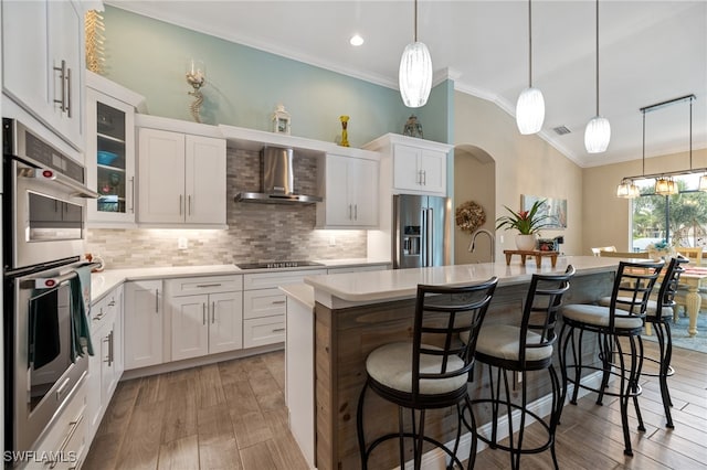 kitchen featuring a center island, stainless steel appliances, wall chimney range hood, a breakfast bar area, and white cabinets