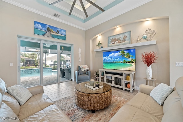 living room featuring built in features, ornamental molding, ceiling fan, a raised ceiling, and light wood-type flooring