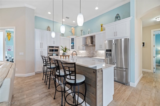 kitchen with pendant lighting, wall chimney range hood, stainless steel appliances, and white cabinets