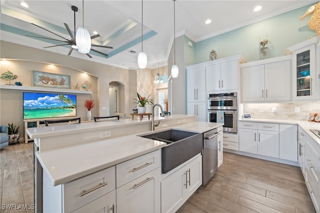 kitchen with white cabinets, hanging light fixtures, ornamental molding, a kitchen island with sink, and stainless steel appliances