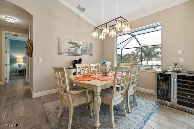 dining room featuring ornamental molding, lofted ceiling, wine cooler, and light hardwood / wood-style flooring