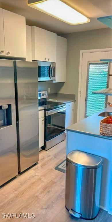 kitchen featuring white cabinetry, sink, light wood-type flooring, and appliances with stainless steel finishes