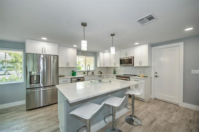 kitchen featuring appliances with stainless steel finishes, a kitchen island, white cabinets, decorative light fixtures, and sink