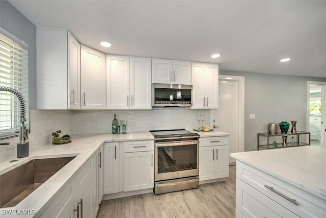 kitchen featuring stainless steel appliances, sink, light hardwood / wood-style flooring, white cabinetry, and backsplash