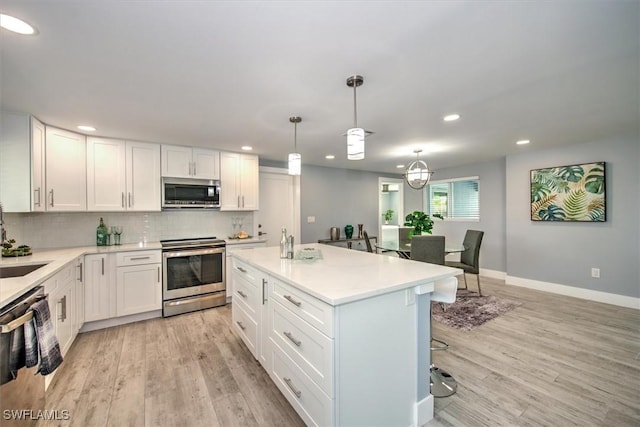 kitchen featuring white cabinetry, stainless steel appliances, pendant lighting, a kitchen island, and light hardwood / wood-style flooring