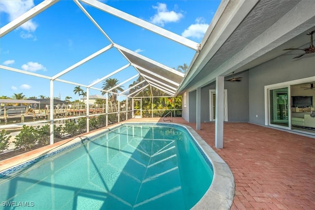 view of pool with a lanai, ceiling fan, a water view, and a patio