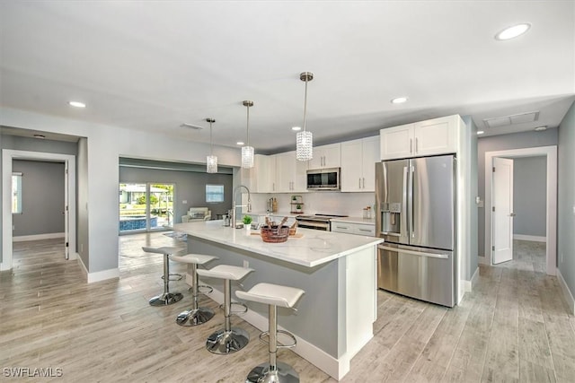 kitchen featuring decorative light fixtures, a kitchen island with sink, white cabinets, appliances with stainless steel finishes, and a kitchen breakfast bar