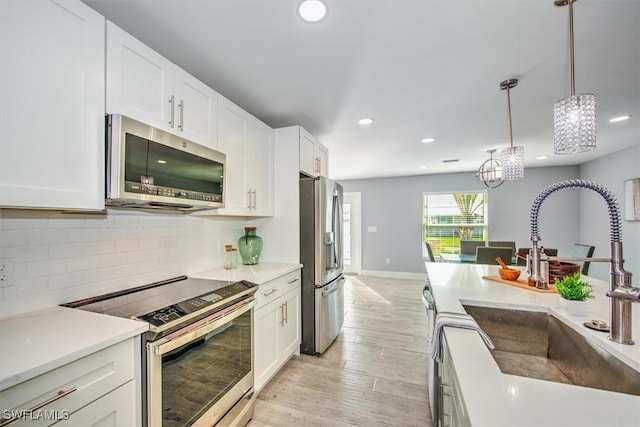 kitchen featuring sink, white cabinetry, light wood-type flooring, hanging light fixtures, and appliances with stainless steel finishes