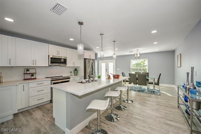 kitchen with white cabinets, stainless steel appliances, decorative light fixtures, and a center island with sink