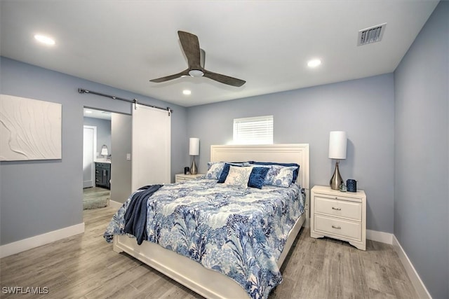 bedroom with connected bathroom, ceiling fan, a barn door, and light hardwood / wood-style flooring