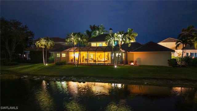 view of front of property with a water view, glass enclosure, and a lawn