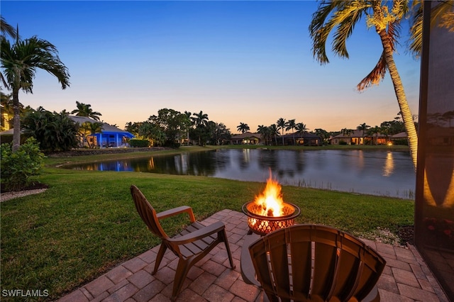 patio terrace at dusk featuring a water view, a lawn, and a fire pit