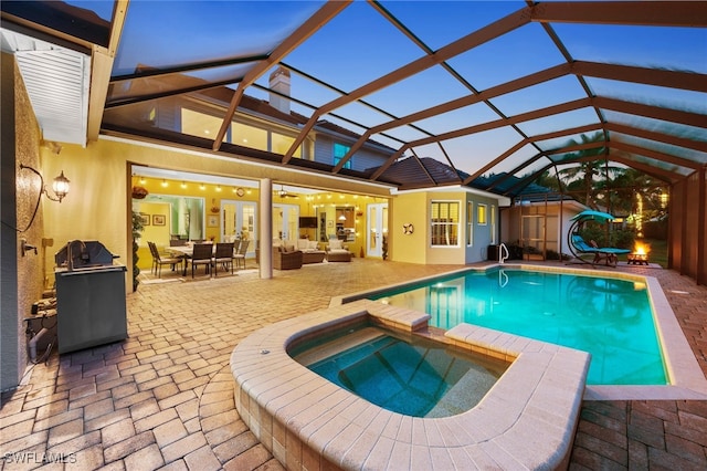 pool at dusk featuring glass enclosure, a pool with connected hot tub, a patio area, and outdoor lounge area