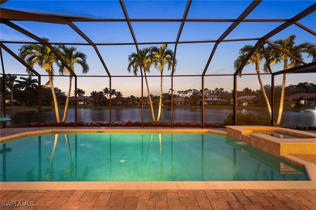 pool at dusk with a water view, glass enclosure, and a pool with connected hot tub