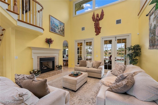 living area featuring french doors, visible vents, a towering ceiling, and a tiled fireplace