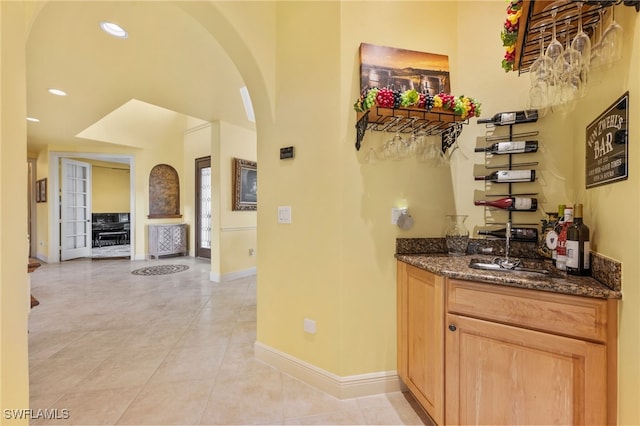 bar featuring arched walkways, light tile patterned flooring, a sink, baseboards, and indoor wet bar