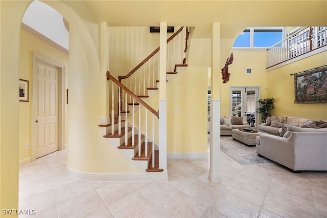 staircase with tile patterned flooring, a high ceiling, baseboards, and arched walkways