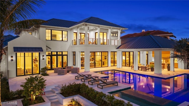 back of house at twilight with a balcony, a standing seam roof, outdoor lounge area, metal roof, and a patio