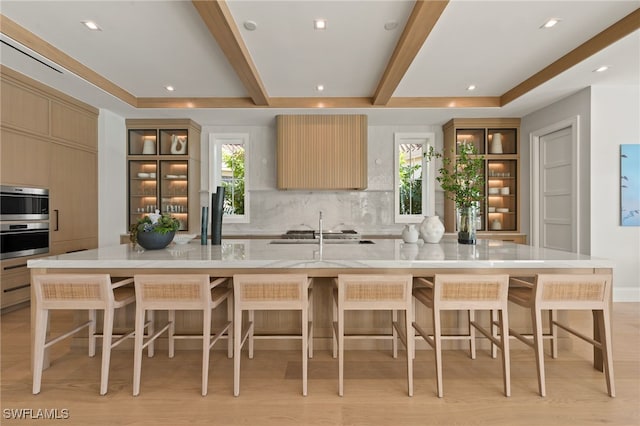 kitchen featuring a large island with sink, backsplash, a kitchen bar, and light hardwood / wood-style flooring