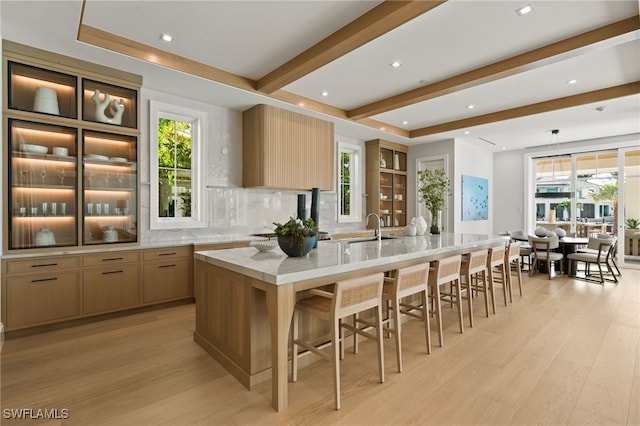 kitchen featuring light hardwood / wood-style flooring, a breakfast bar, a kitchen island with sink, light brown cabinetry, and decorative backsplash