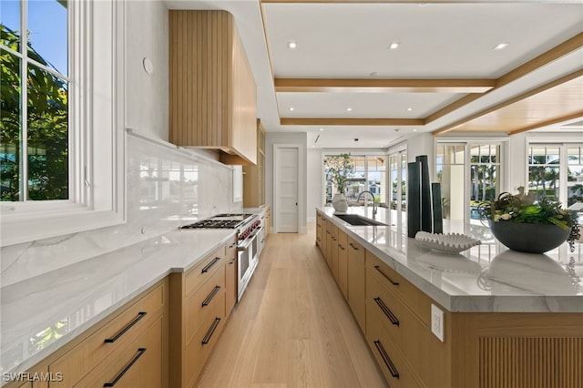 kitchen featuring sink, decorative backsplash, a large island with sink, range with two ovens, and light brown cabinets