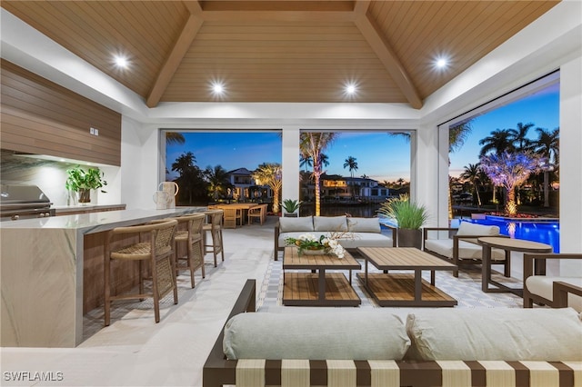 patio terrace at dusk with exterior kitchen, outdoor lounge area, area for grilling, and an outdoor bar