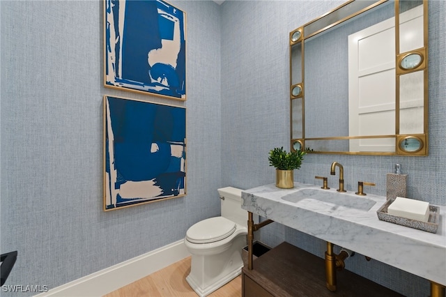 half bathroom with wood finished floors, toilet, a sink, and baseboards
