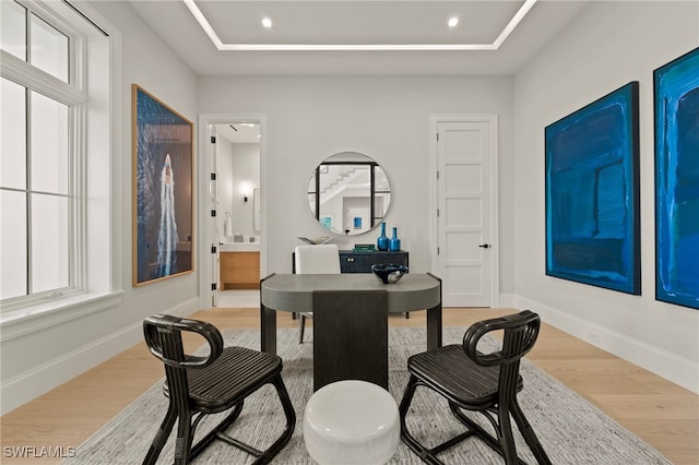 office area with a raised ceiling, a healthy amount of sunlight, and light hardwood / wood-style floors