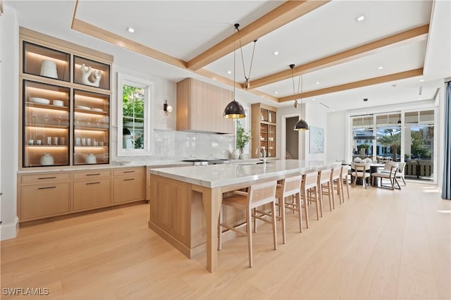 kitchen featuring light brown cabinetry, light wood-style flooring, decorative backsplash, a sink, and recessed lighting