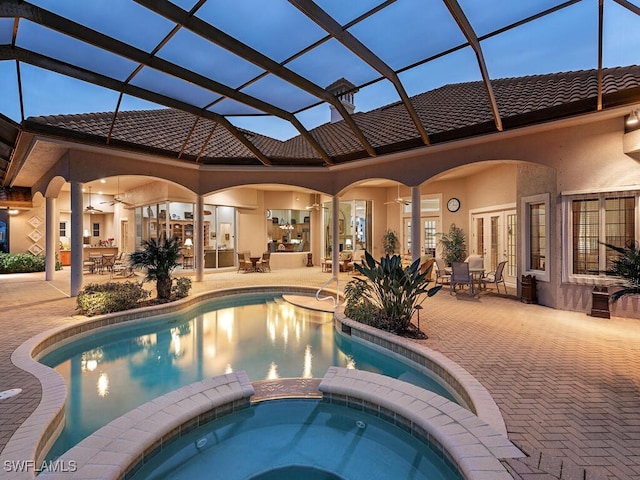 pool at dusk featuring french doors, an in ground hot tub, a lanai, and a patio