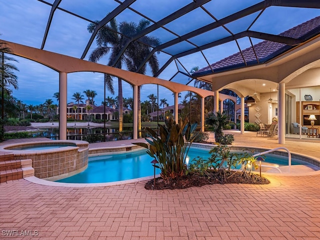 pool at dusk with an in ground hot tub, a patio, and glass enclosure