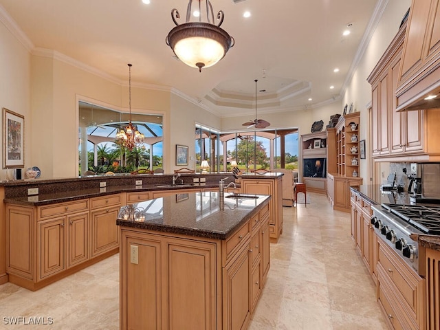 kitchen featuring stainless steel gas stovetop, a kitchen island with sink, dark stone counters, and decorative light fixtures