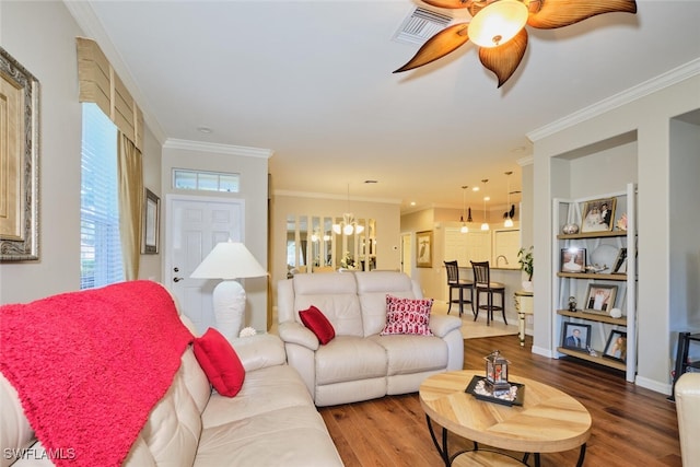 living room featuring built in features, crown molding, ceiling fan with notable chandelier, and wood-type flooring