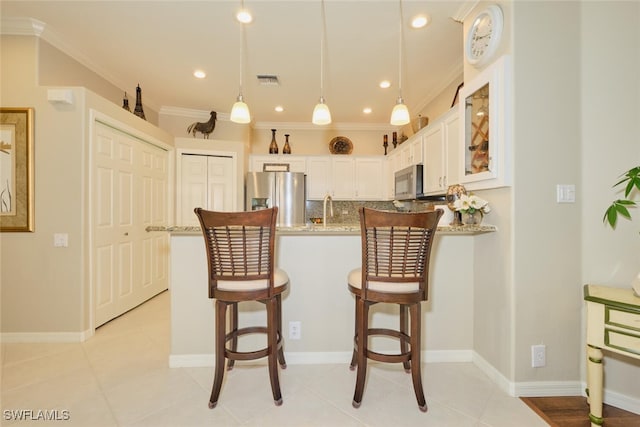 kitchen featuring light stone counters, hanging light fixtures, white cabinetry, appliances with stainless steel finishes, and ornamental molding