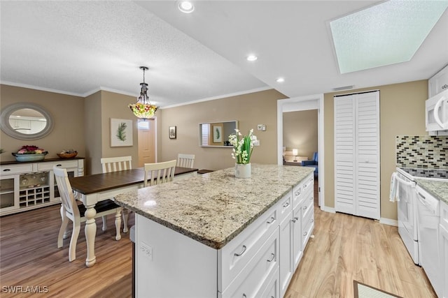 kitchen with tasteful backsplash, white appliances, hanging light fixtures, white cabinets, and a center island