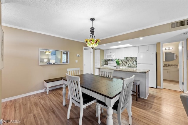 dining area with a textured ceiling, crown molding, light hardwood / wood-style floors, and sink