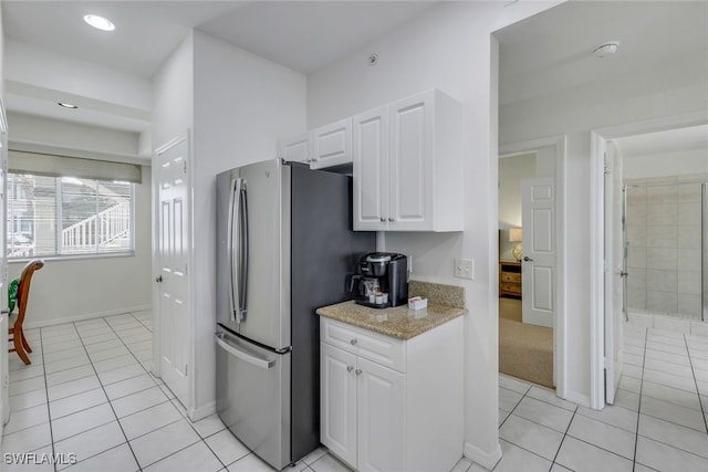 kitchen with light tile patterned floors, white cabinets, light stone counters, and stainless steel fridge