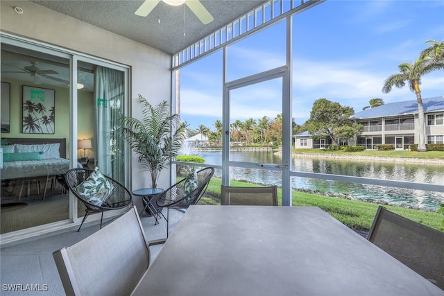 sunroom with ceiling fan and a water view