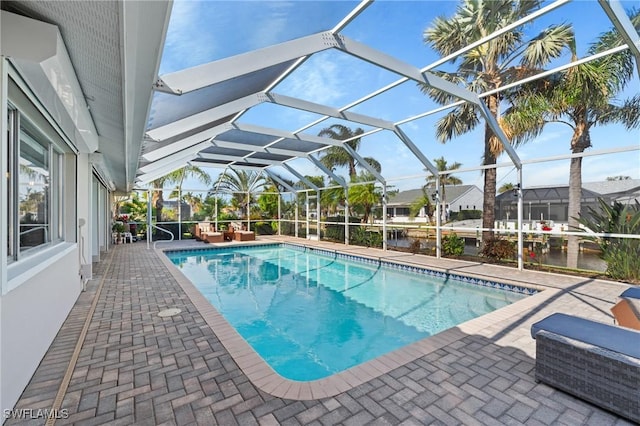 view of pool featuring glass enclosure, a water view, and a patio