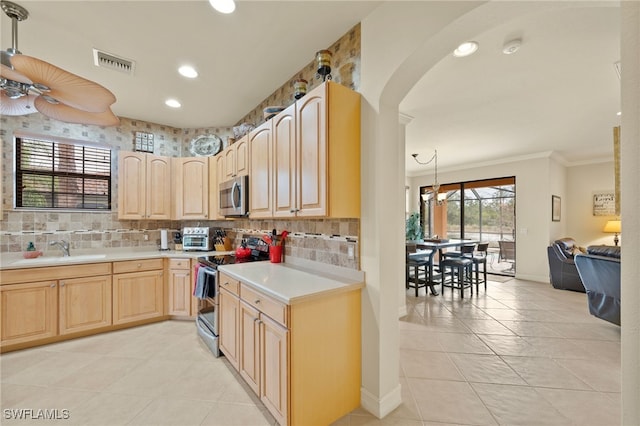 kitchen with stainless steel appliances, light brown cabinetry, hanging light fixtures, and sink