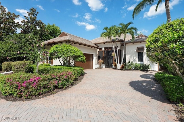 view of front of home with a tiled roof, decorative driveway, a garage, and stucco siding