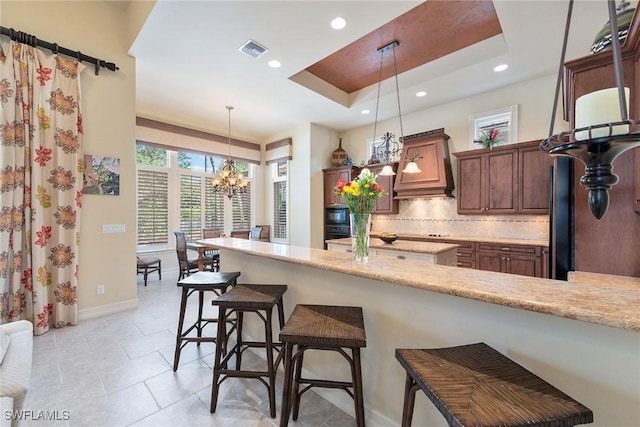 kitchen with visible vents, a breakfast bar, a tray ceiling, backsplash, and custom exhaust hood