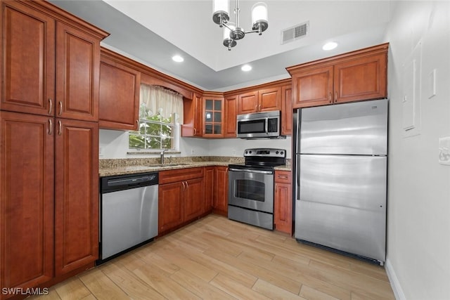 kitchen featuring sink, a chandelier, light stone counters, stainless steel appliances, and light wood-type flooring