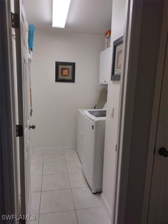 clothes washing area with washing machine and dryer, cabinets, and light tile patterned floors