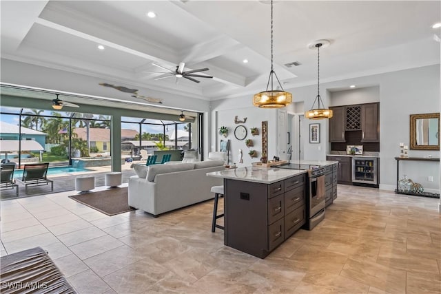 kitchen with stainless steel range with electric stovetop, a center island with sink, wine cooler, pendant lighting, and beamed ceiling